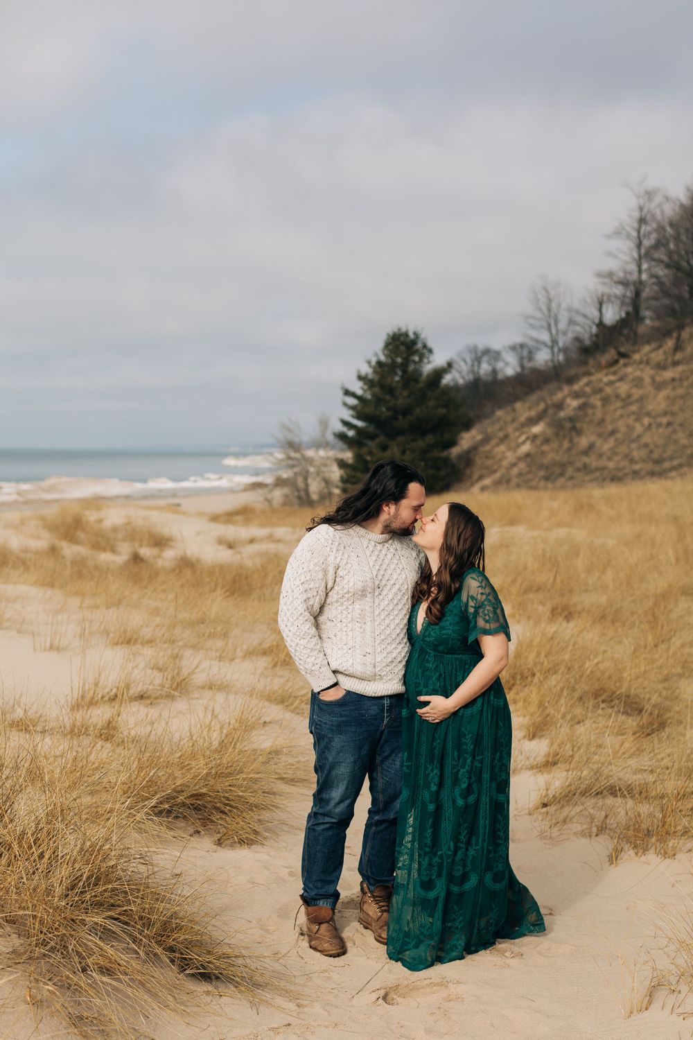 Couple in dressy attire share intimate moment on beach with dunes.