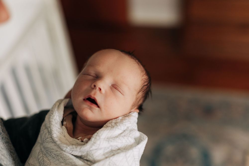 Close-up of a sleeping newborn baby wrapped in a white blanket.