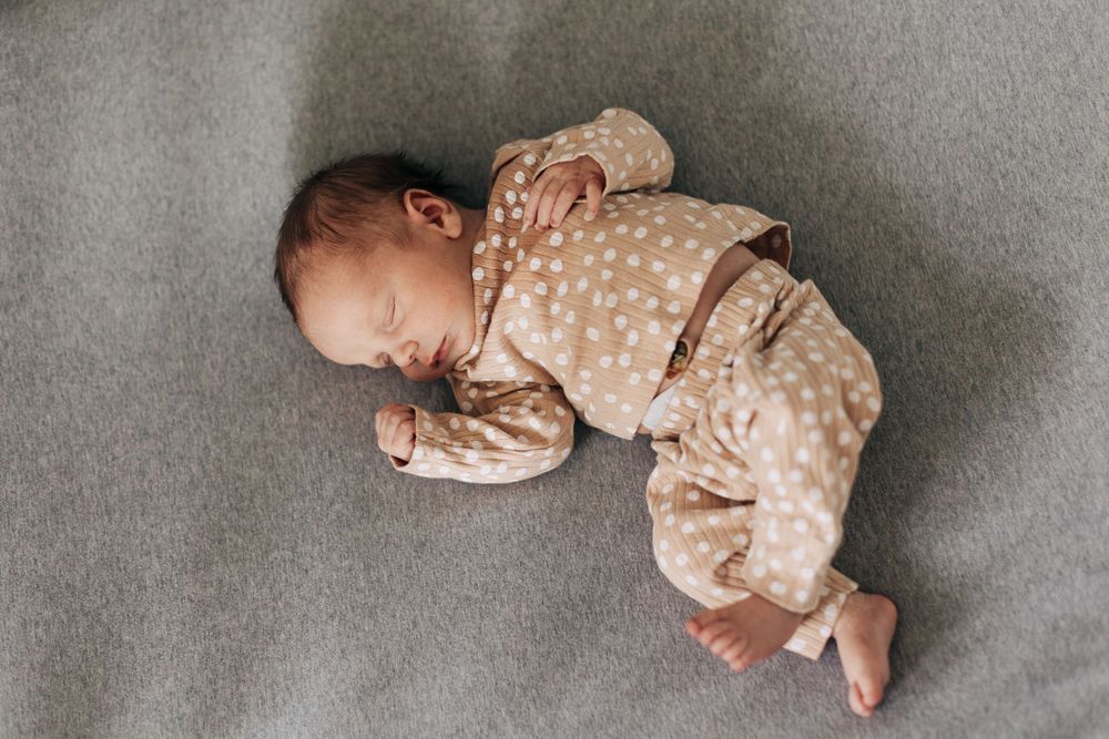 Sleeping baby in polka dot onesie lying peacefully on grey blanket.