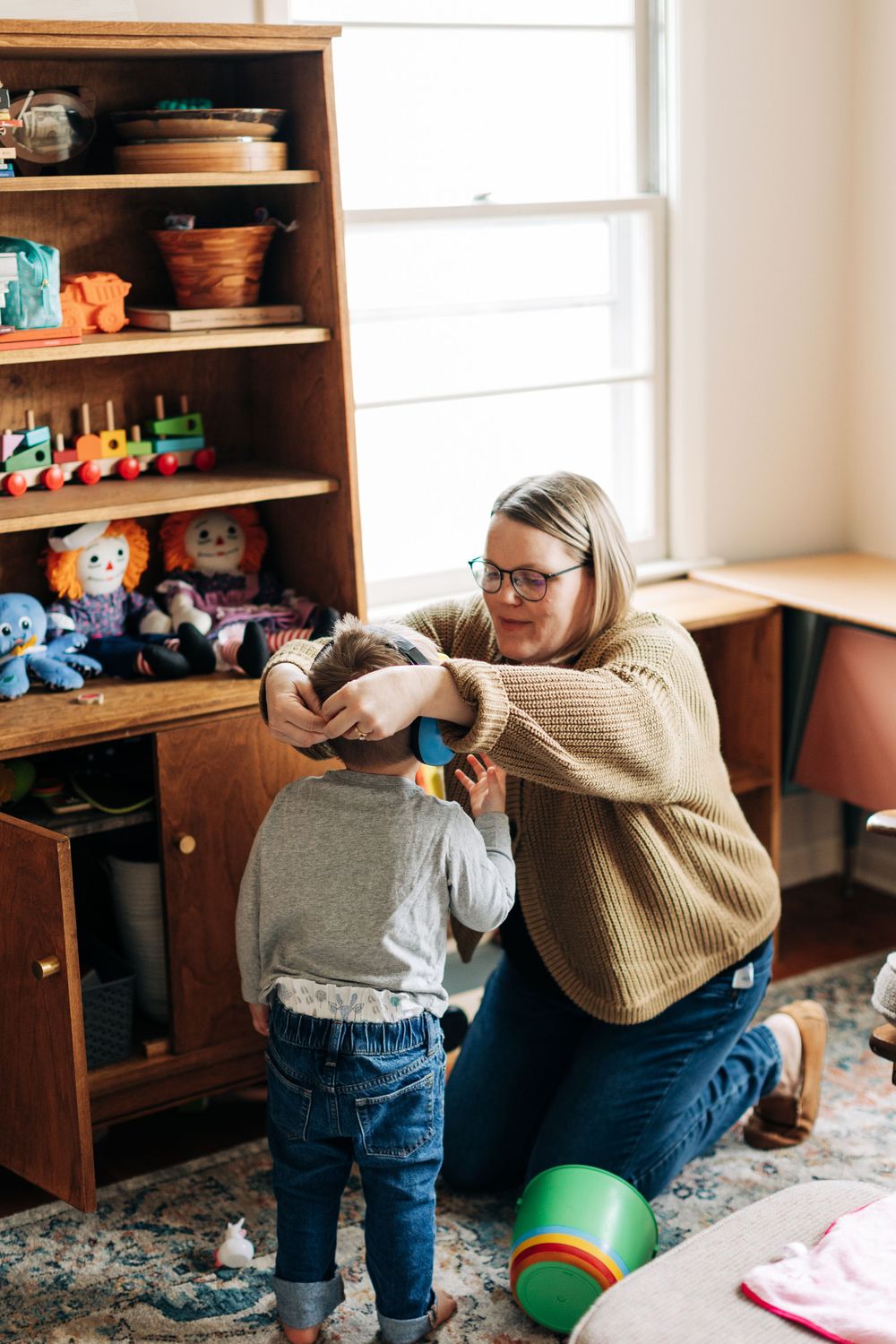 Sweet interaction by wooden toy shelf with chunky knit sweater and jeans.
