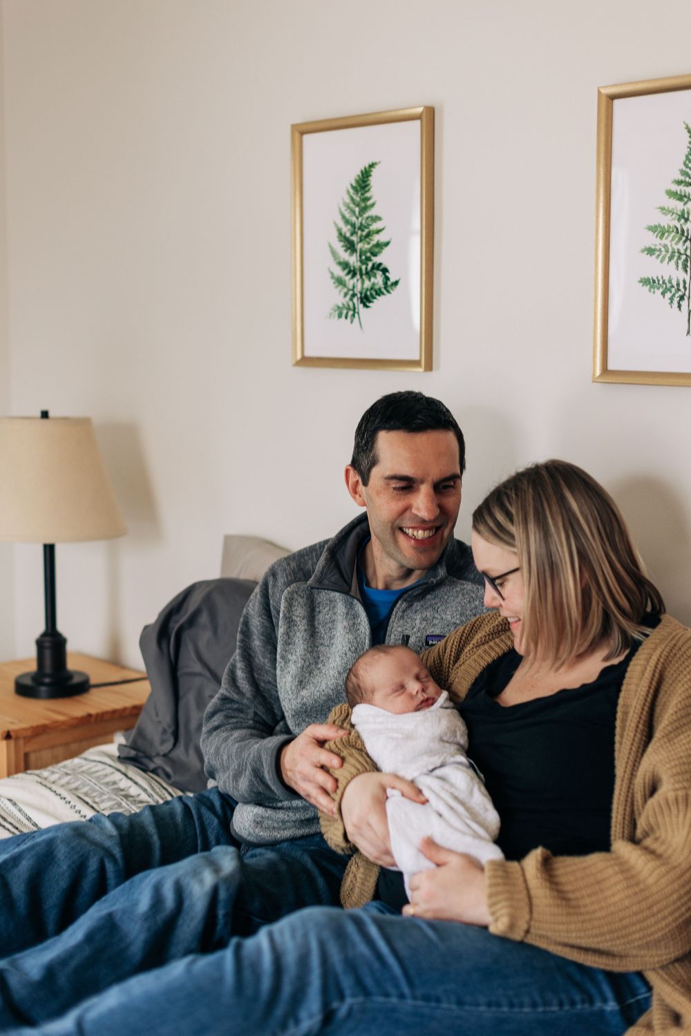 Intimate family moment on bed with botanical prints hanging on wall.