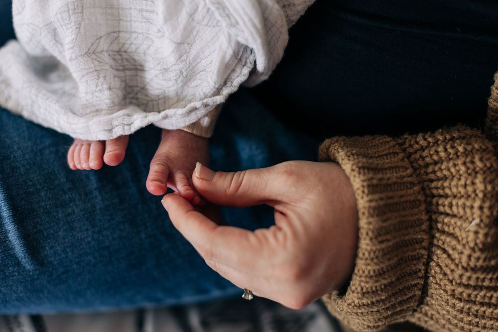 Close-up of gentle hand holding tiny baby fingers against dark fabric.