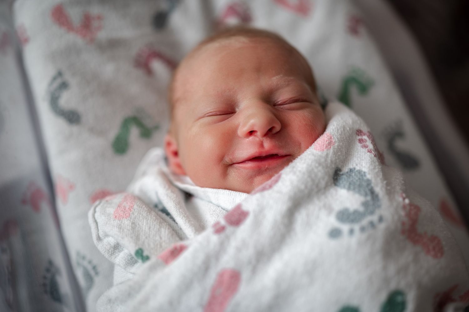 Newborn smiling wrapped in a blanket in the hospital at a fresh 48 photoshoot session Palm Bay Brevard Melbourne Cocoa Beach Vero Florida