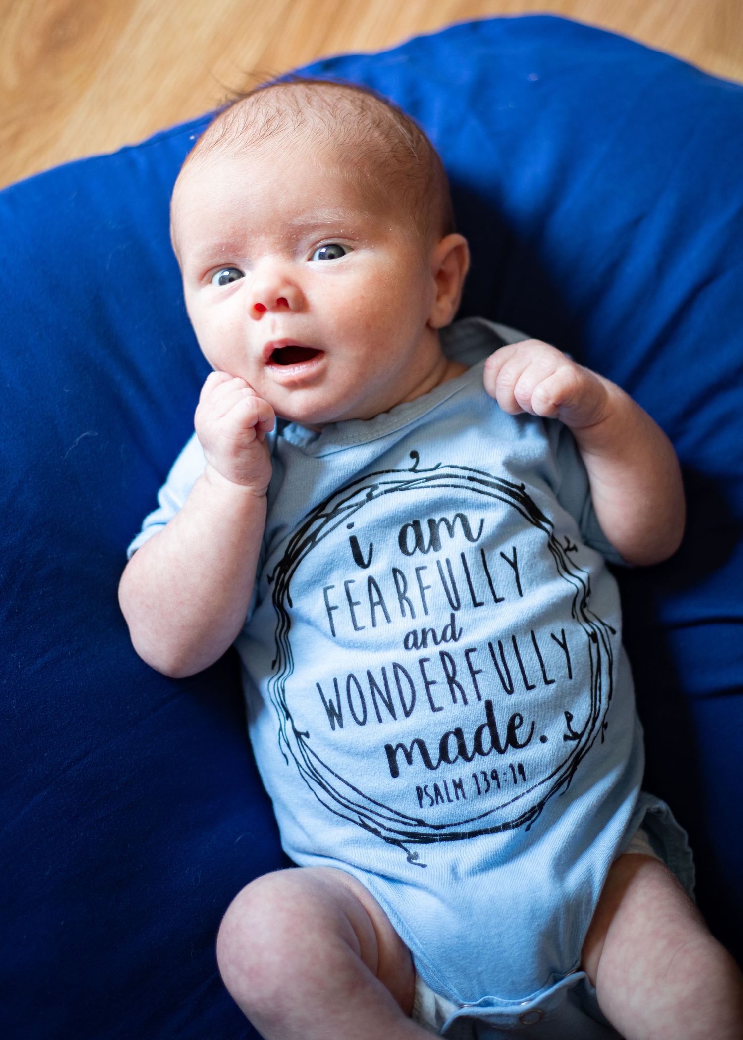 Newborn baby in light blue onesie reading Fearfully and Wonderfully Made Psalm 139.