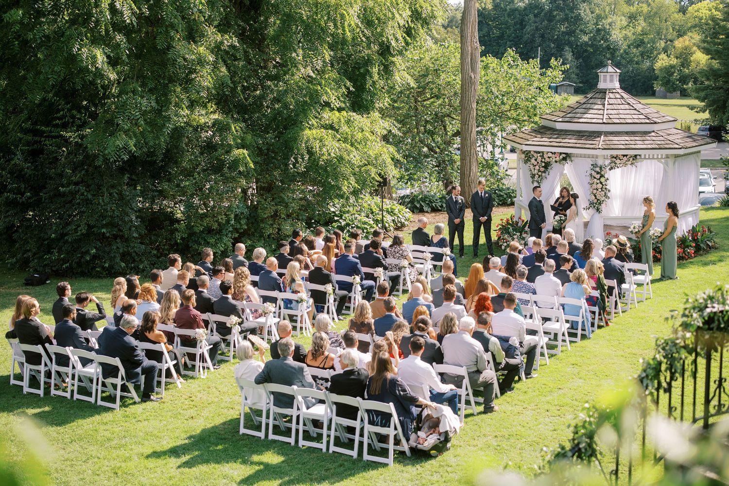 Outdoor garden wedding ceremony setup with white chairs arranged in rows surrounded by lush greenery.