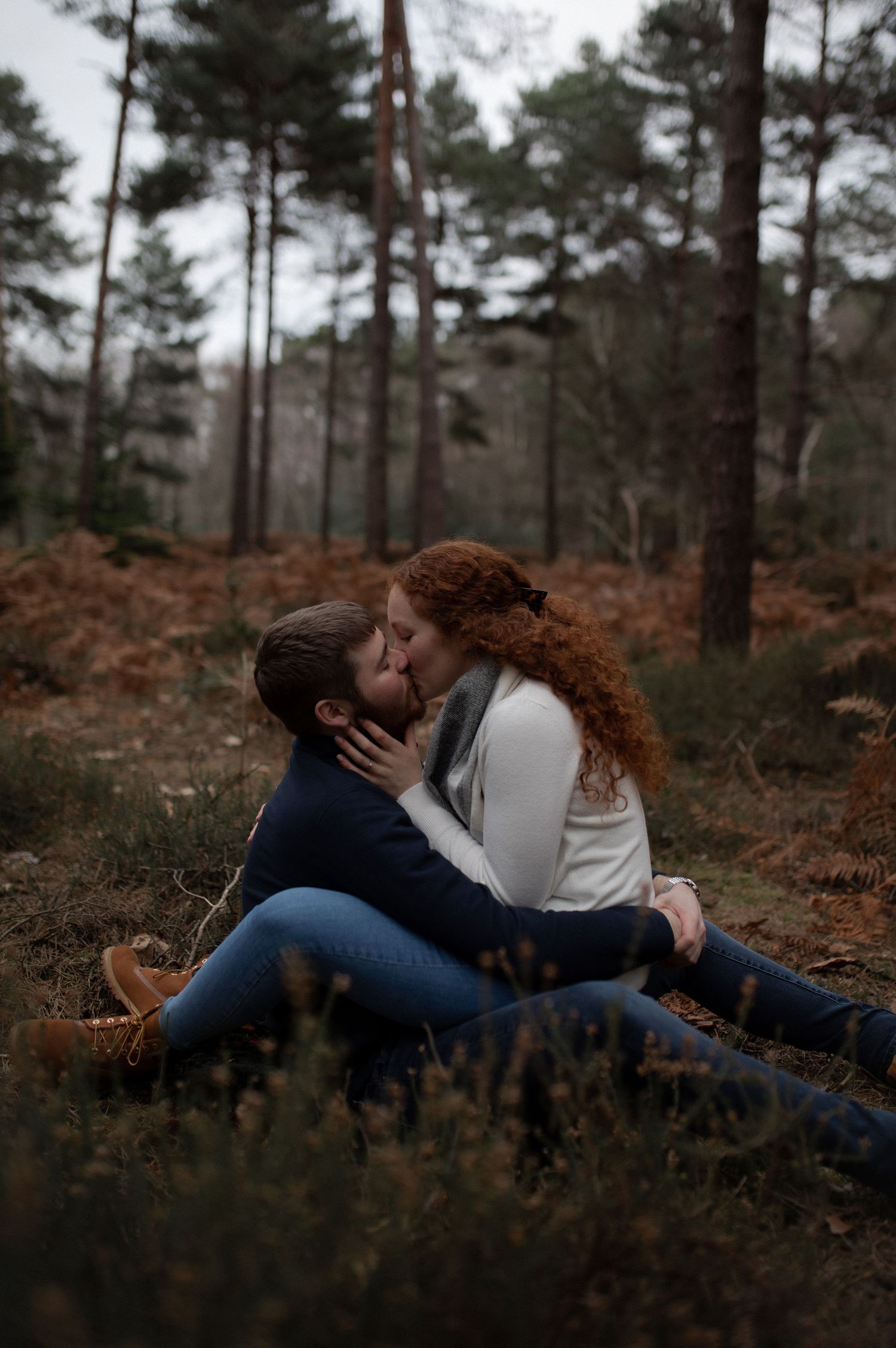 Intimate couple lying together in autumn forest during moody outdoor photoshoot.