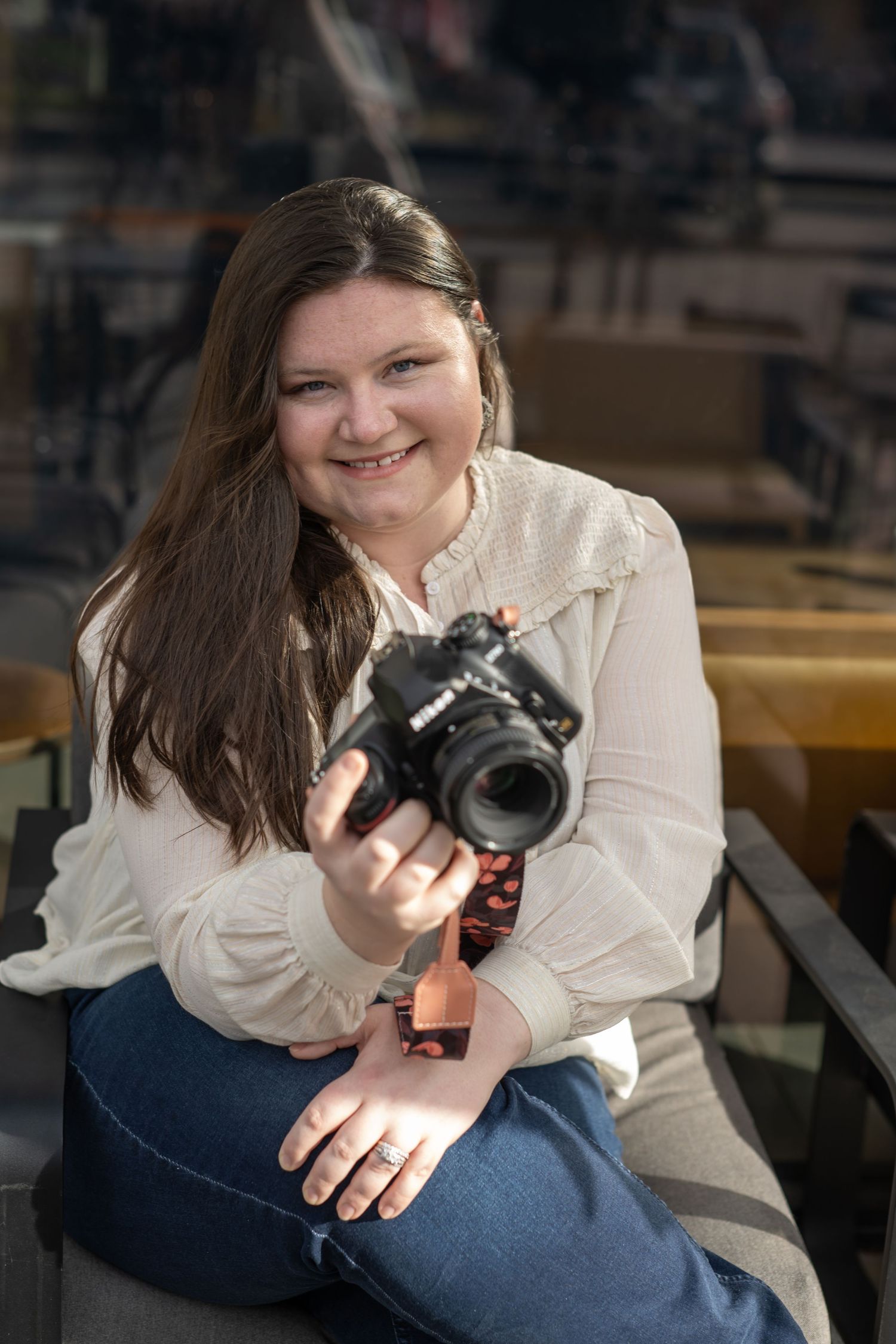 Professional photographer in white blouse sits with camera in indoor setting.