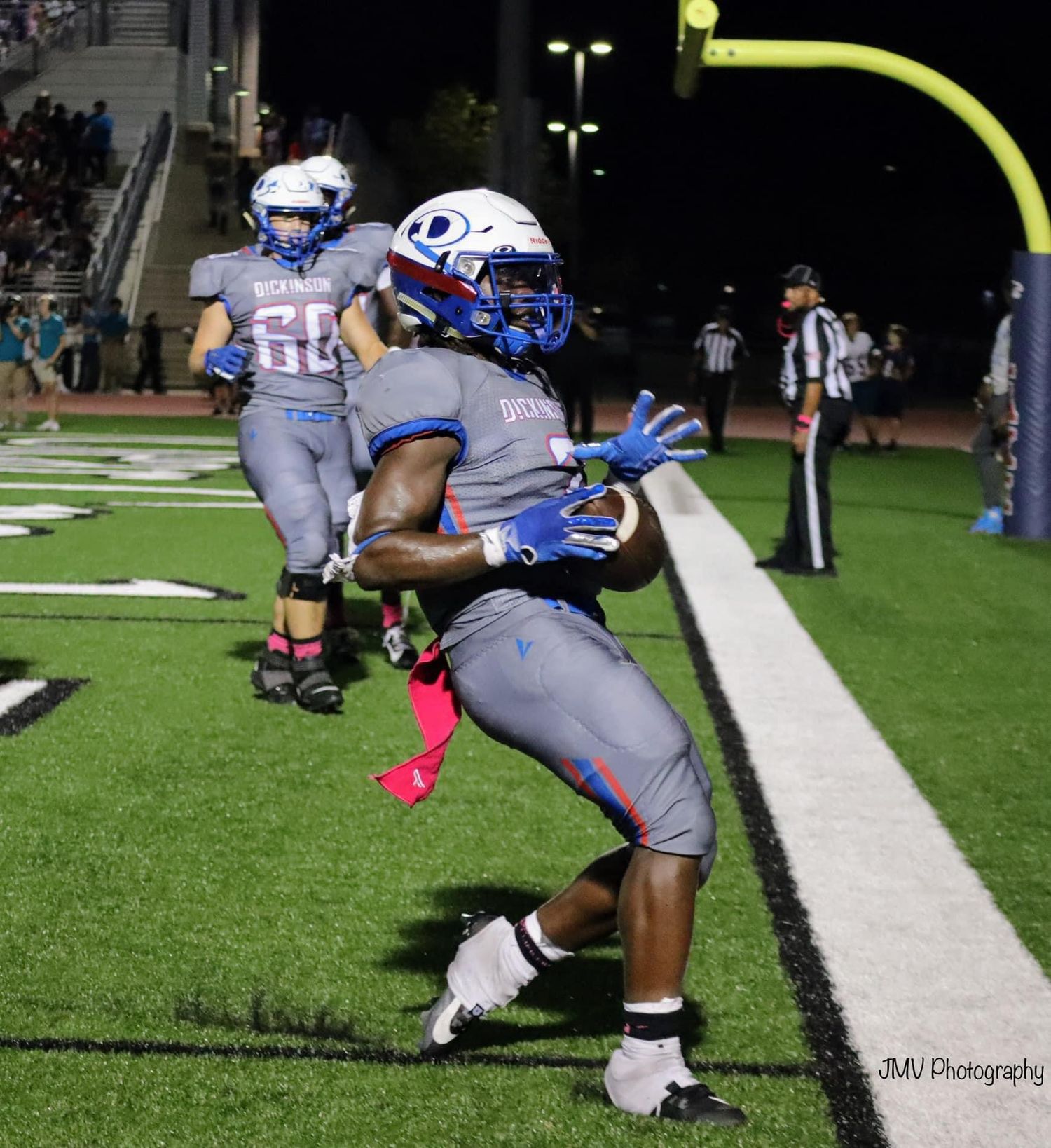 Football player in blue and gray uniform makes a catch near the sideline during a nighttime game.