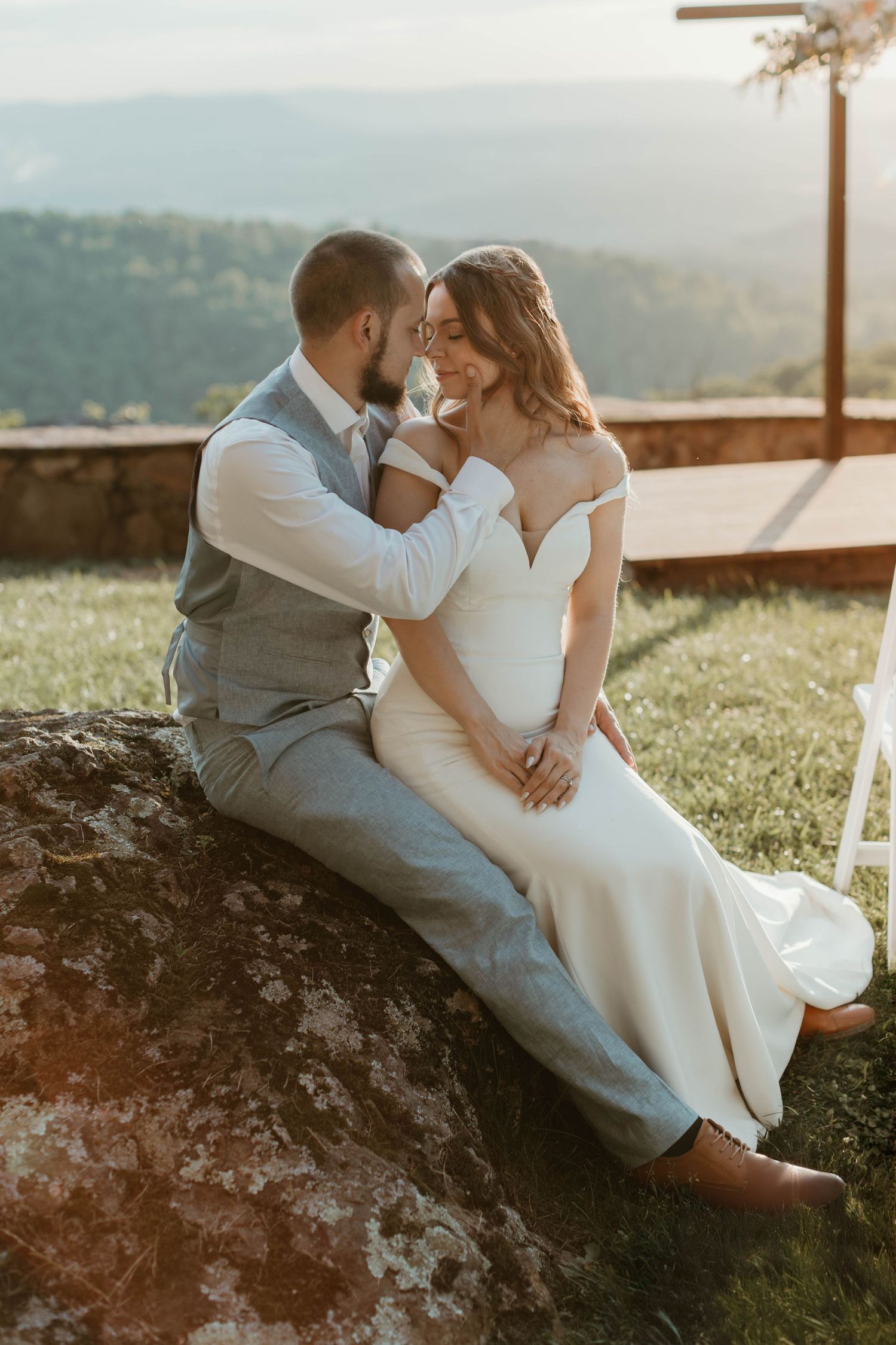 Romantic couple in wedding attire sharing intimate moments on a stone wall at sunset.