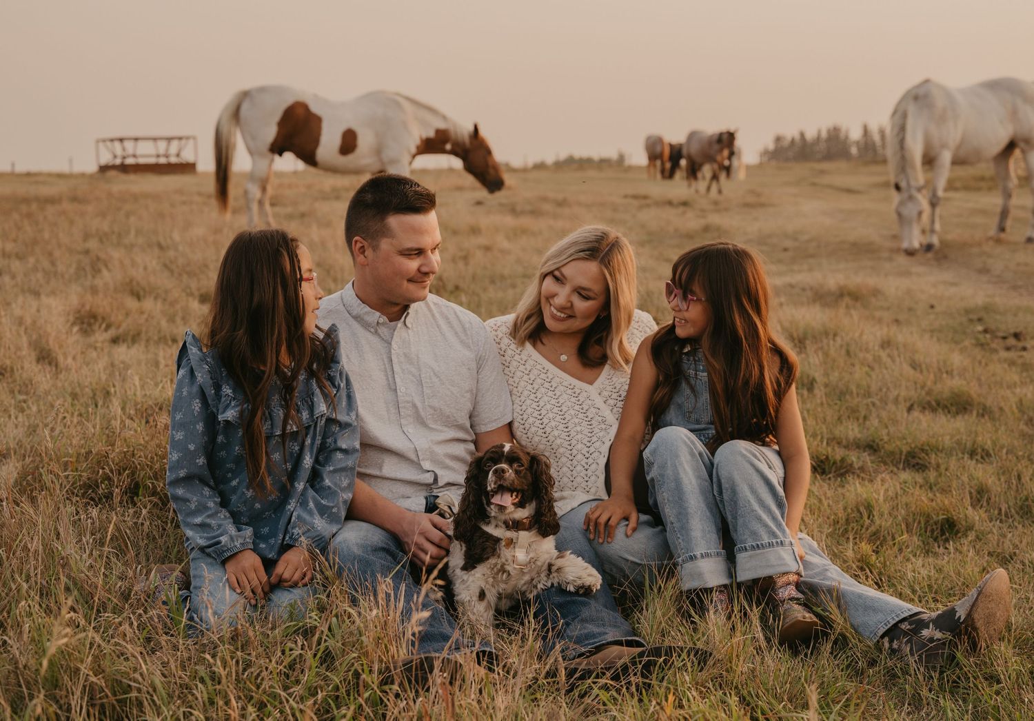 Family shares tender moment in golden wheat field at sunset with small children watching.