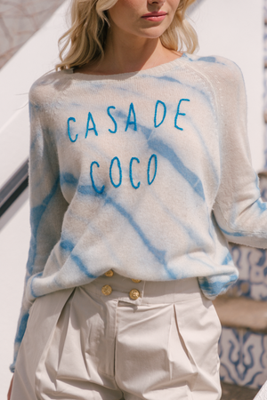 White sweatshirt with blue tie-dye pattern featuring 'CASA DE COCO' text styling.