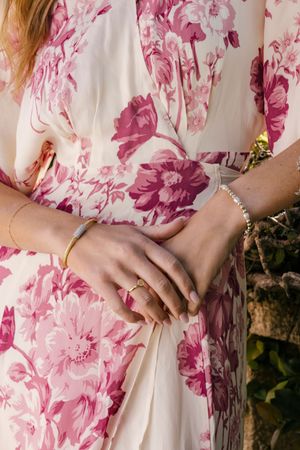 Close-up details of hands against a pink and white floral dress with delicate jewelry accents.