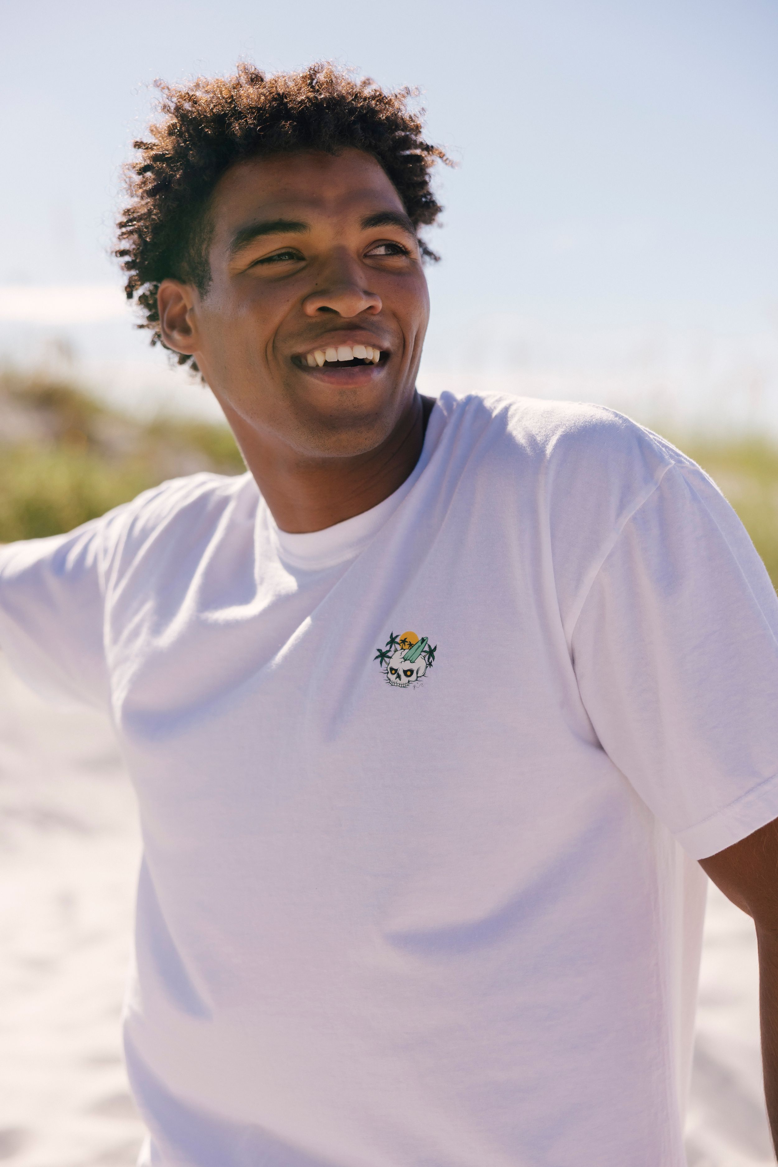 A person in a white t-shirt smiles joyfully while posing outdoors in bright sunlight.