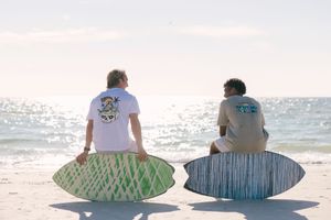 Two people sit side by side on a beach watching the sparkling ocean waves during a sunny day.