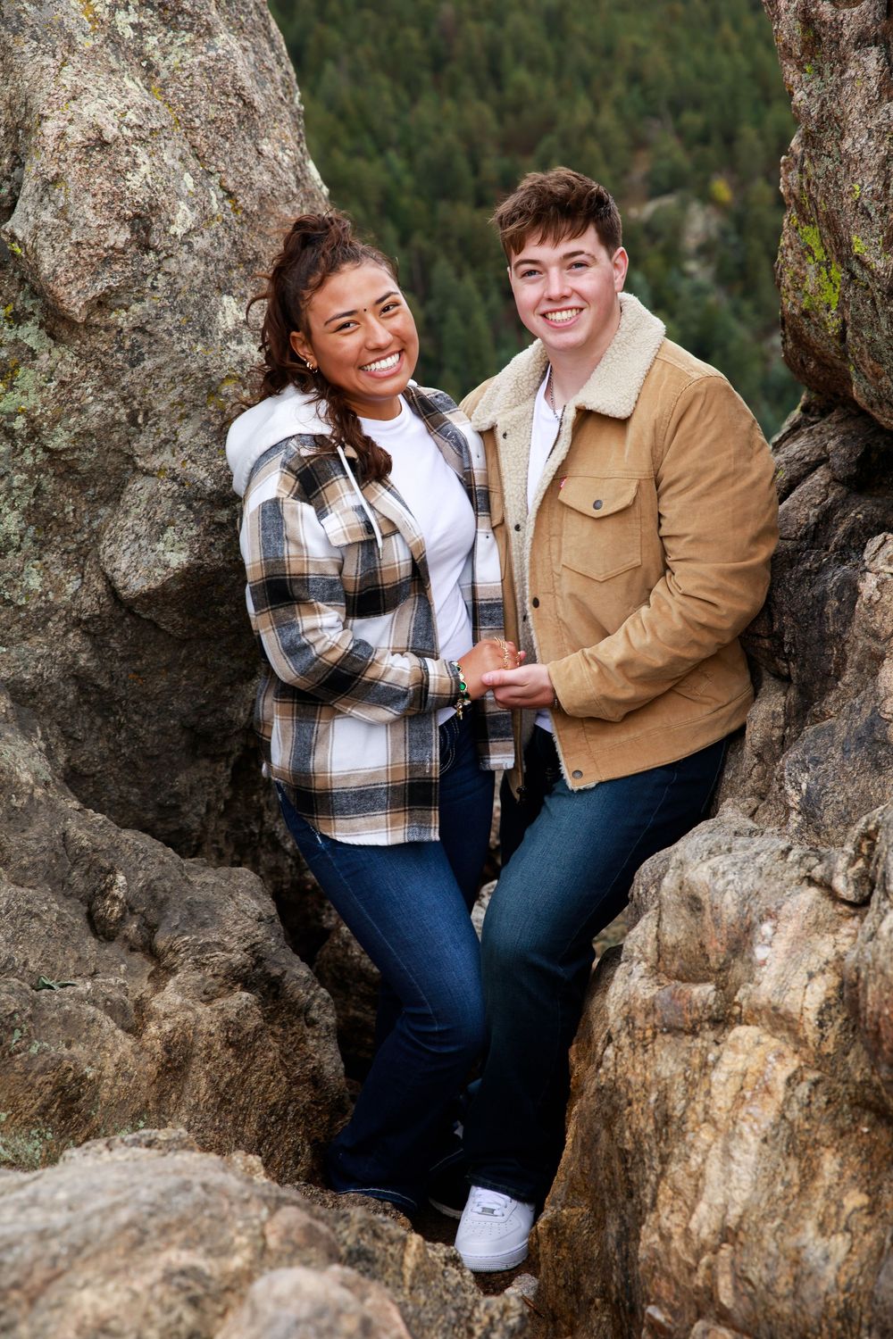 A couple shares joyful moments together while sitting on rocky terrain surrounded by nature.