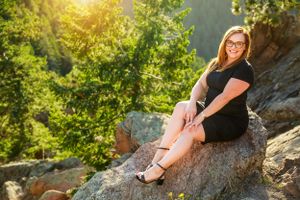 Senior portrait of student sitting on rocky overlook with mountain scenery.