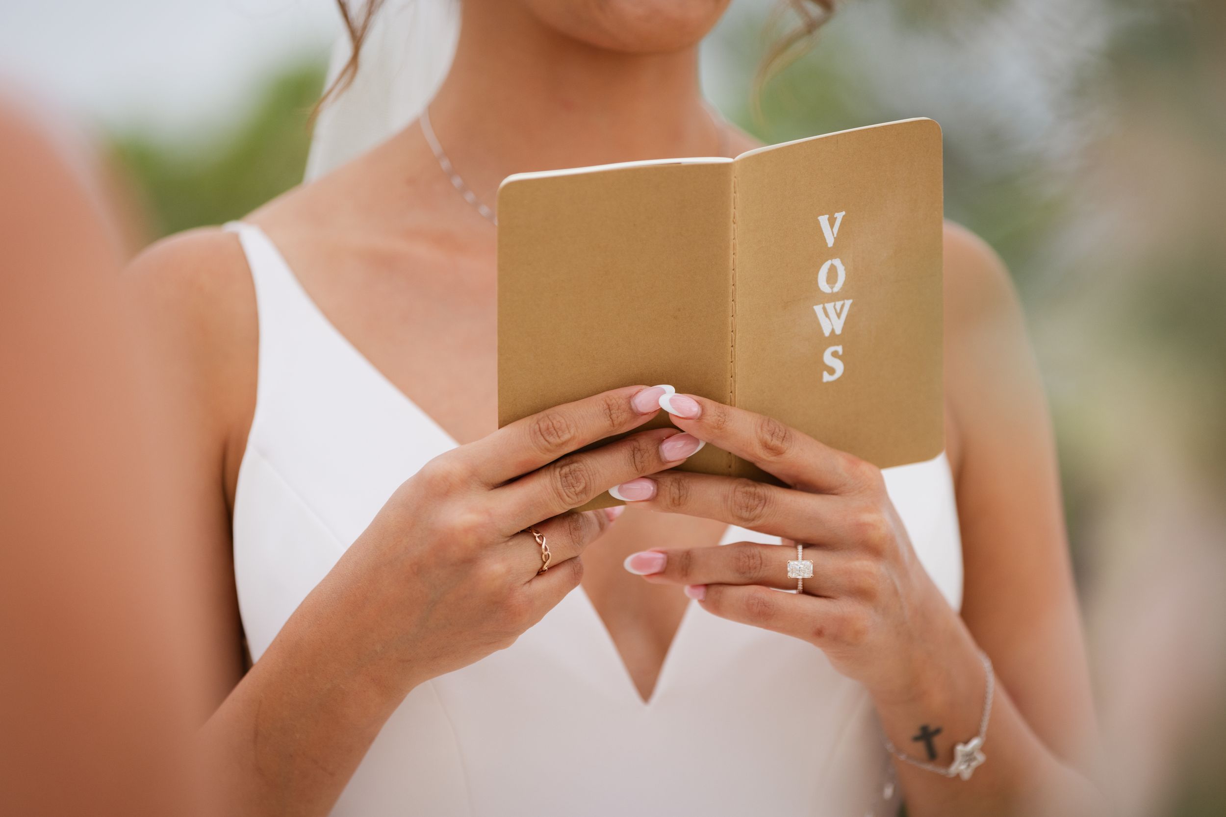 Close-up of a bride holding a gold vow book with VOWS written on the cover.