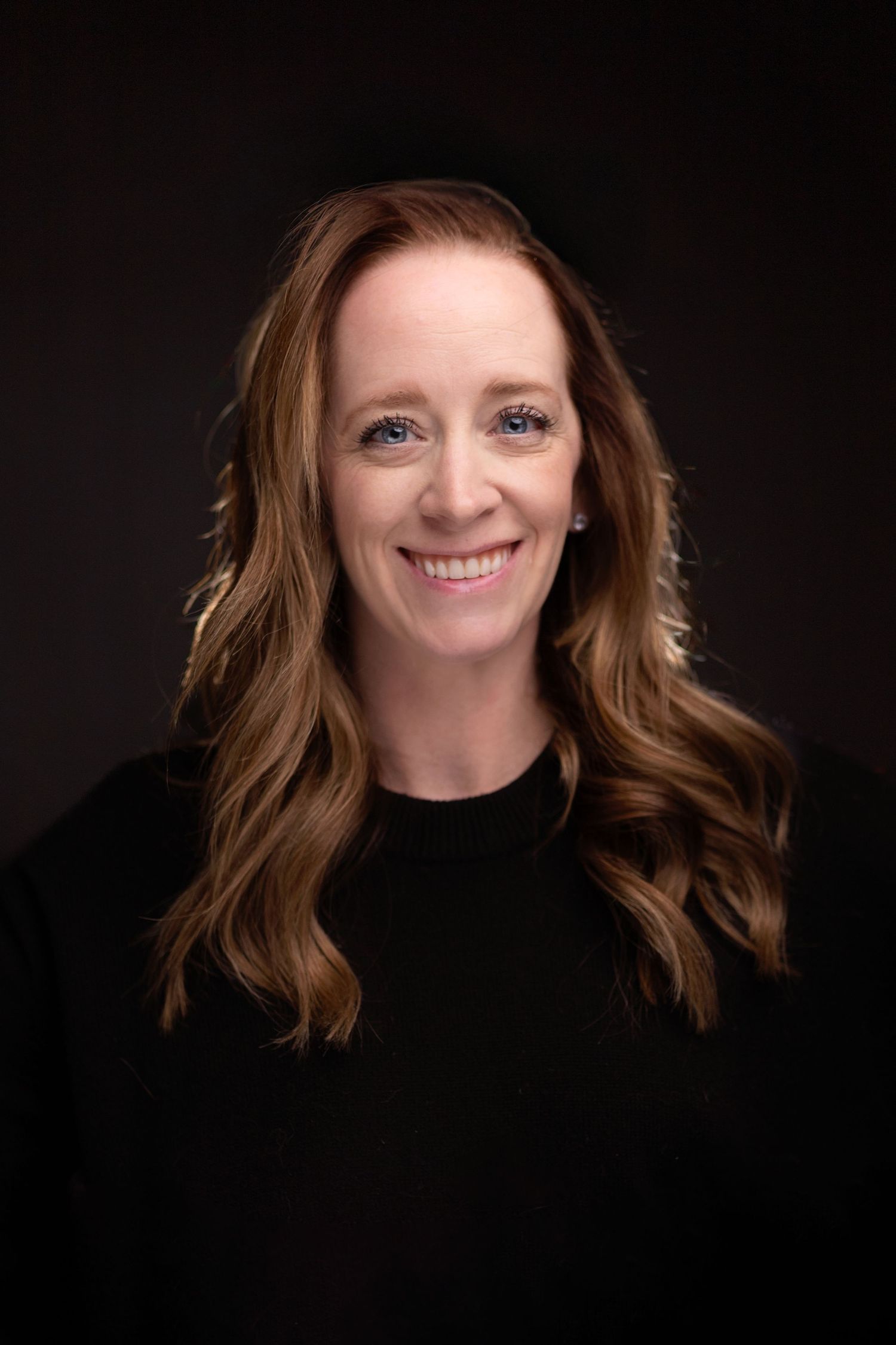 Professional studio portrait against dark background showing woman with wavy brown hair wearing a black sweater. Janesville, WI
Brodhead, WI