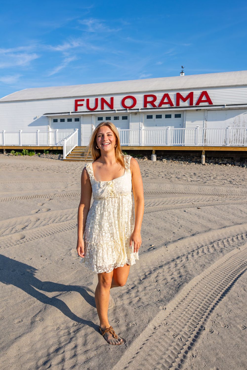 Person in a white dress standing in front of Fun-O-Rama building on a sandy beach.