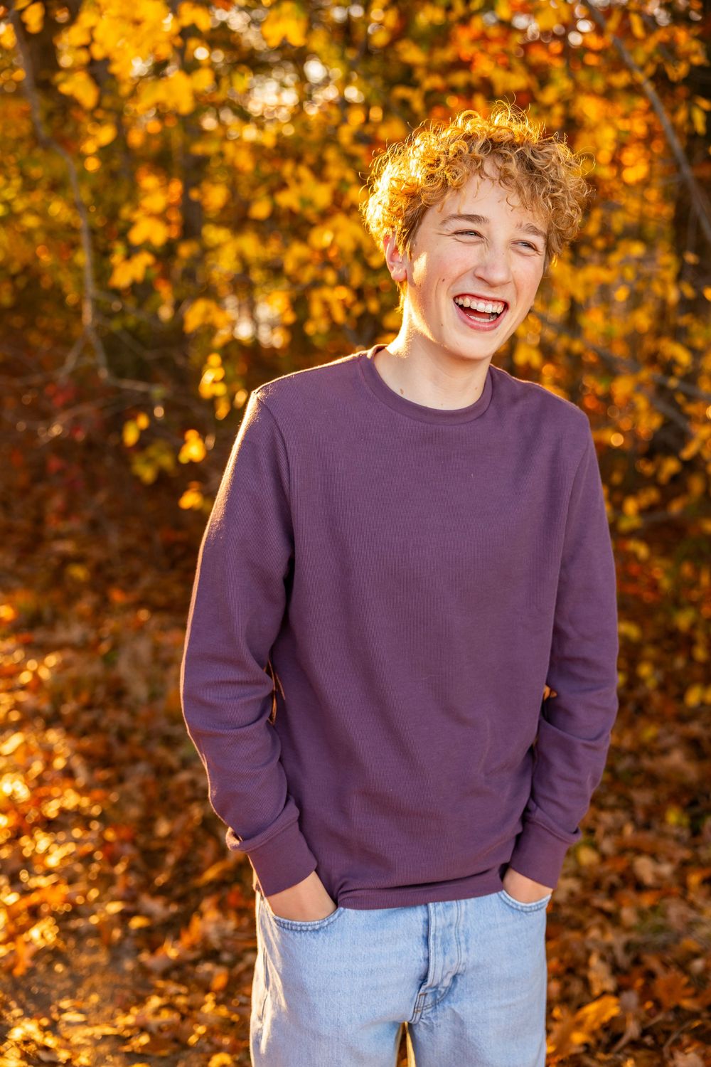 A joyful autumn portrait showing a purple sweater against vibrant golden fall foliage in the background.