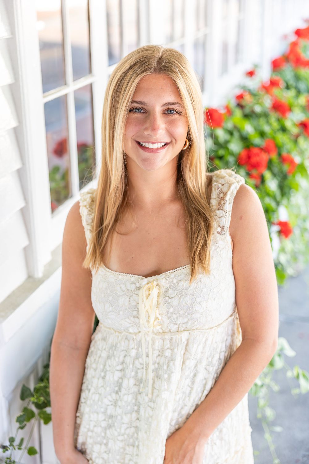 Portrait on a white porch with someone wearing a white lace dress next to red flowers.