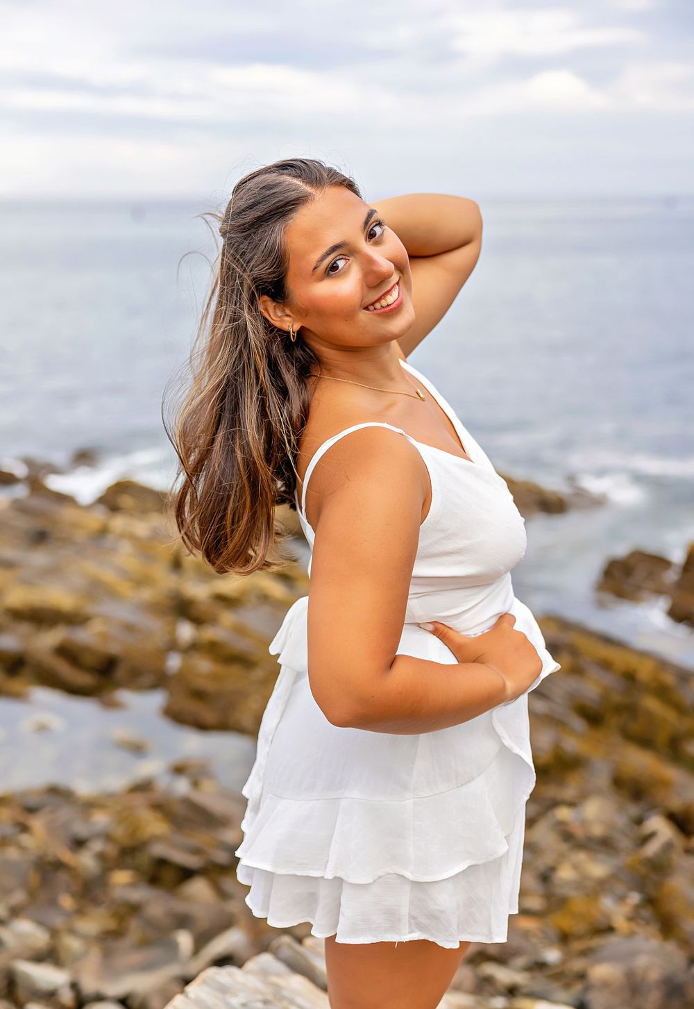 Portrait in a white ruffled dress against a rocky coastal backdrop with ocean views.