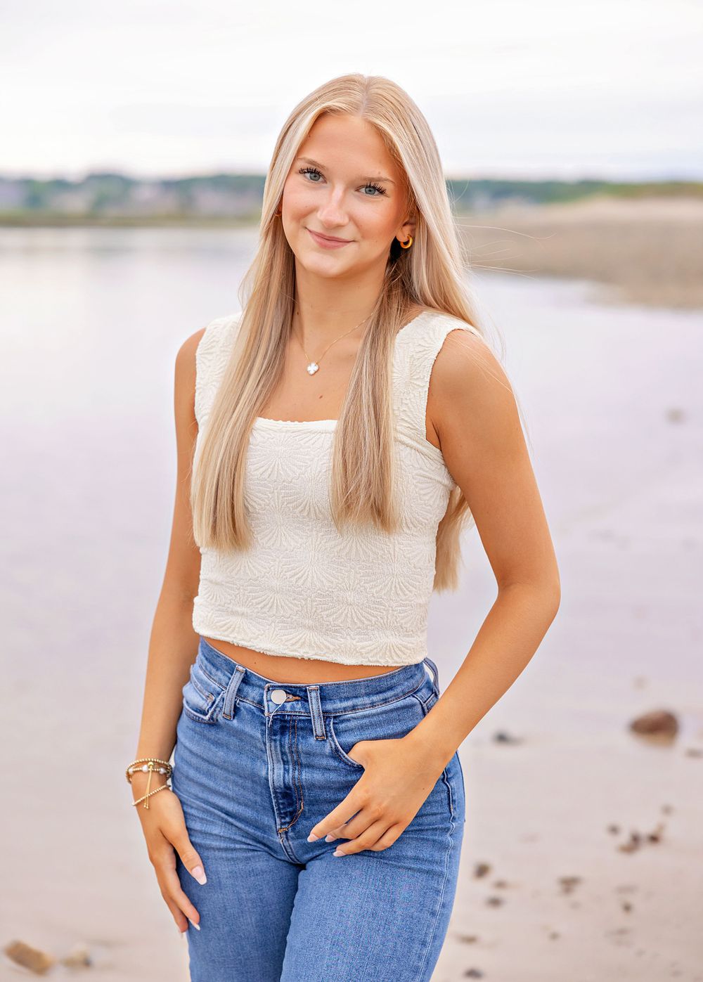 Casual summer portrait by the water wearing a white crop top and high-waisted jeans.