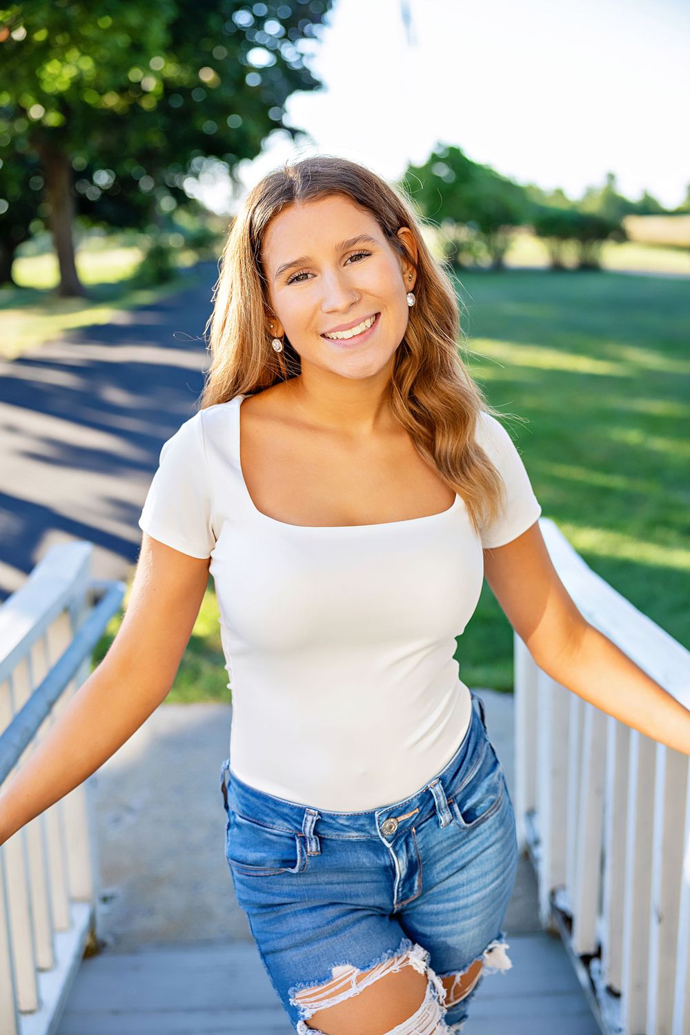 Summer portrait on outdoor stairs wearing a white fitted top and distressed denim jeans.