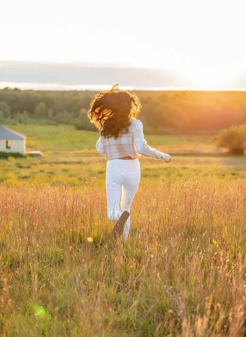 Silhouette of a woman in white clothing dancing in a sun-lit meadow at golden hour.