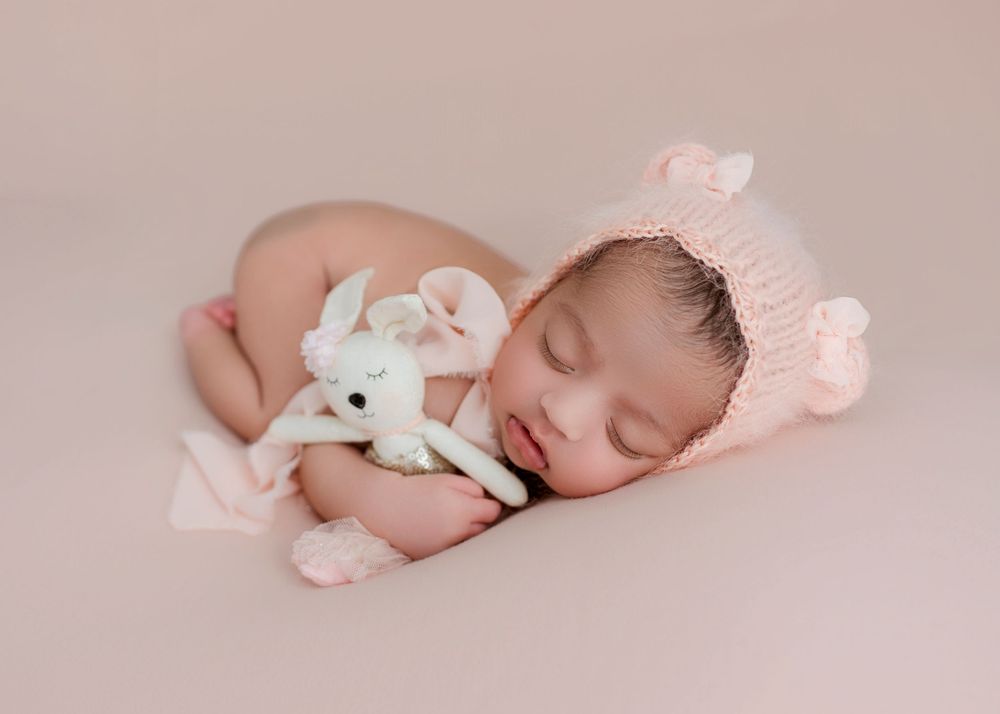 Sleeping newborn baby in soft pink tones with delicate white and pink accessories for professional photography.
