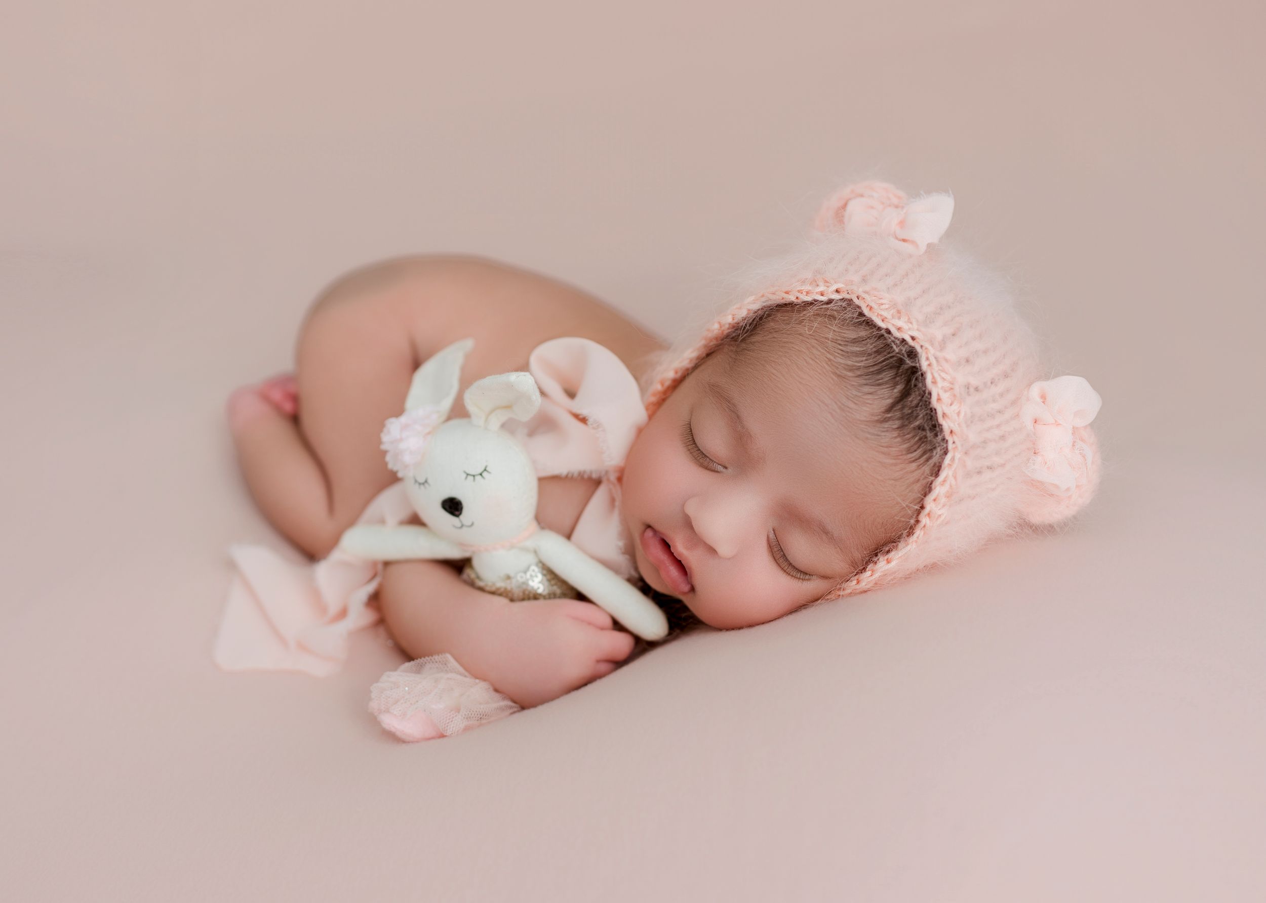 Sleeping newborn baby in soft pink tones with delicate white and pink accessories for professional photography.