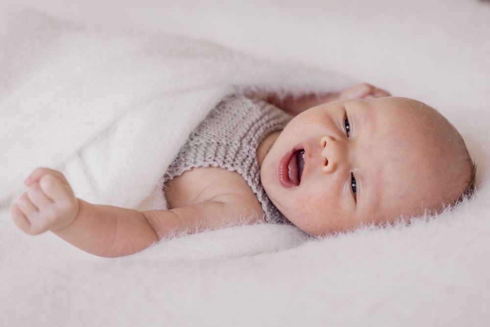 Newborn baby wrapped in knitted blanket lying on white bedding.