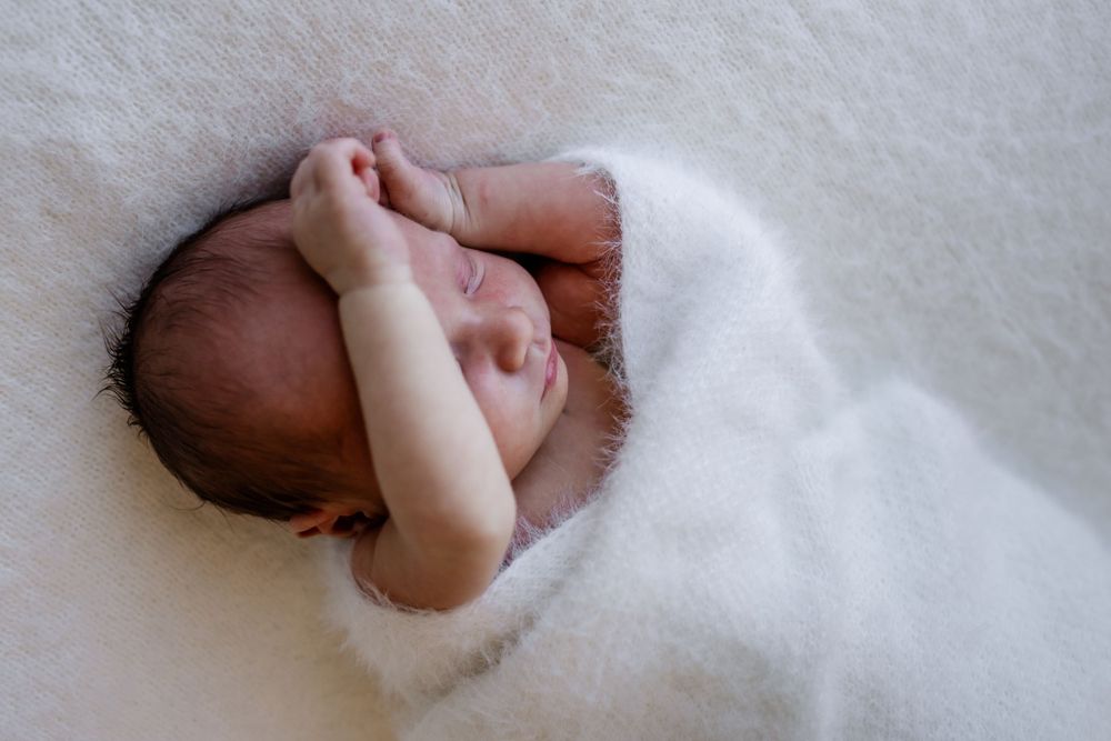 Close-up details of a sleeping newborn wrapped in soft white blankets.