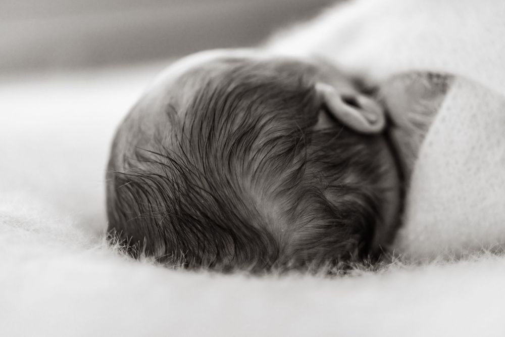 Side profile of sleeping newborn with dark hair against white background.