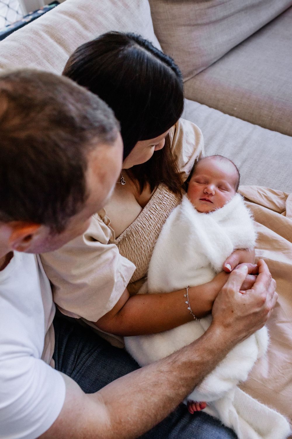 Intimate family moment captured during newborn photography session on couch.