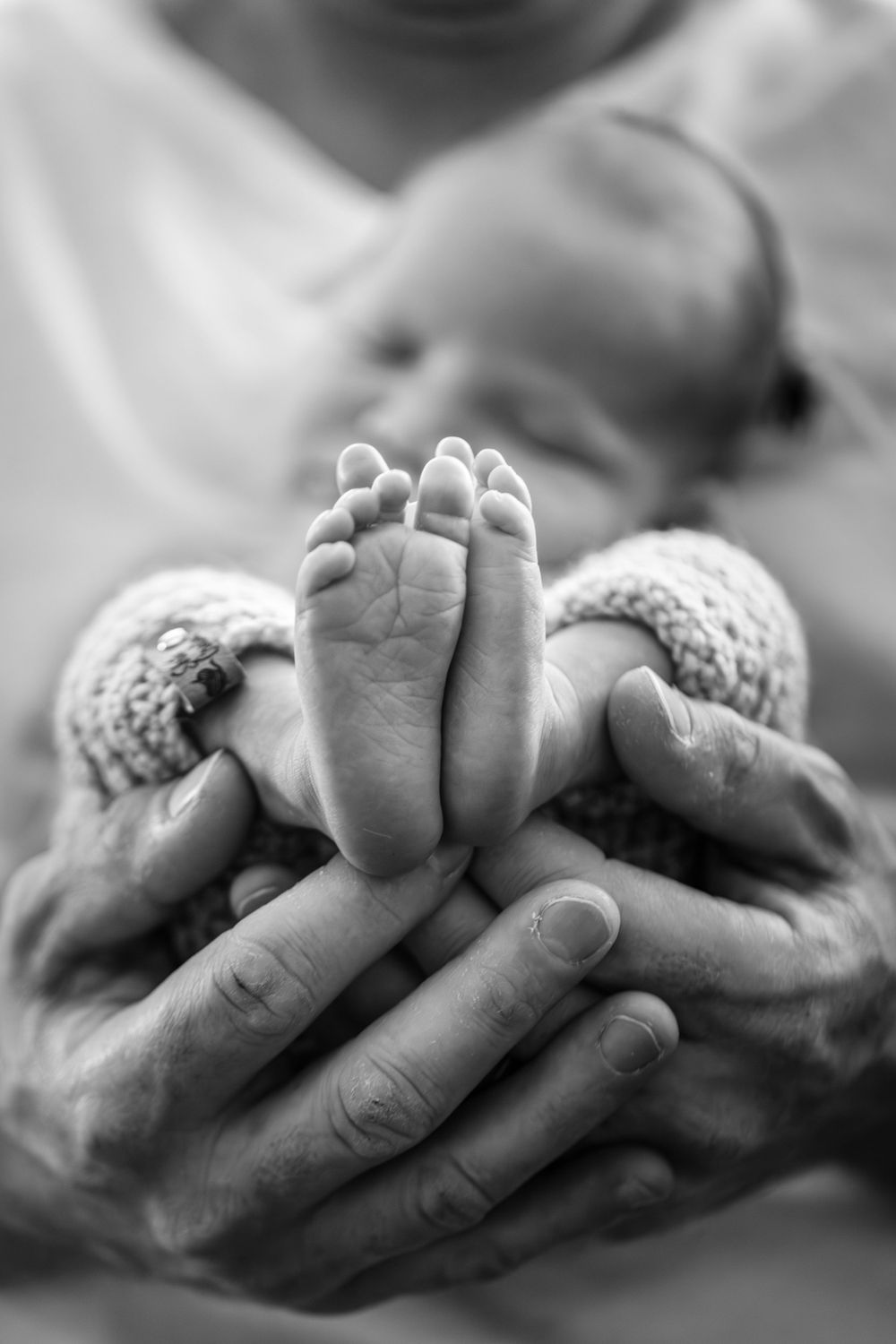 Adult hands gently cradling tiny newborn feet in black and white.