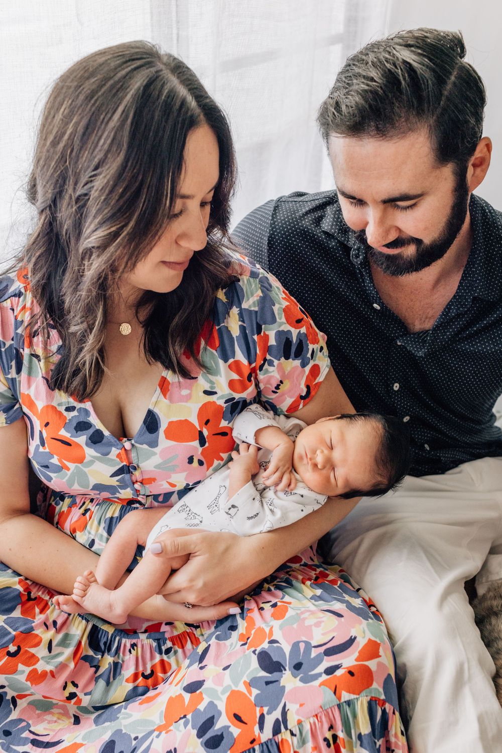A couple in casual attire shares tender moments with their newborn baby on white furniture.