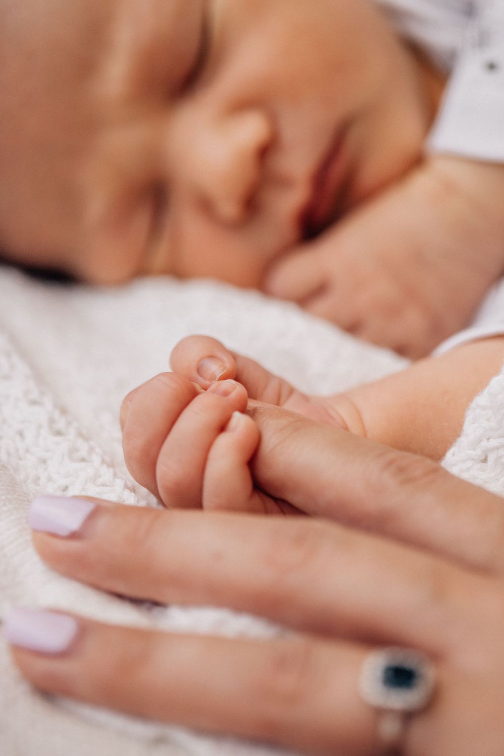 Gentle hands holding newborn's tiny fingers against white lace fabric.