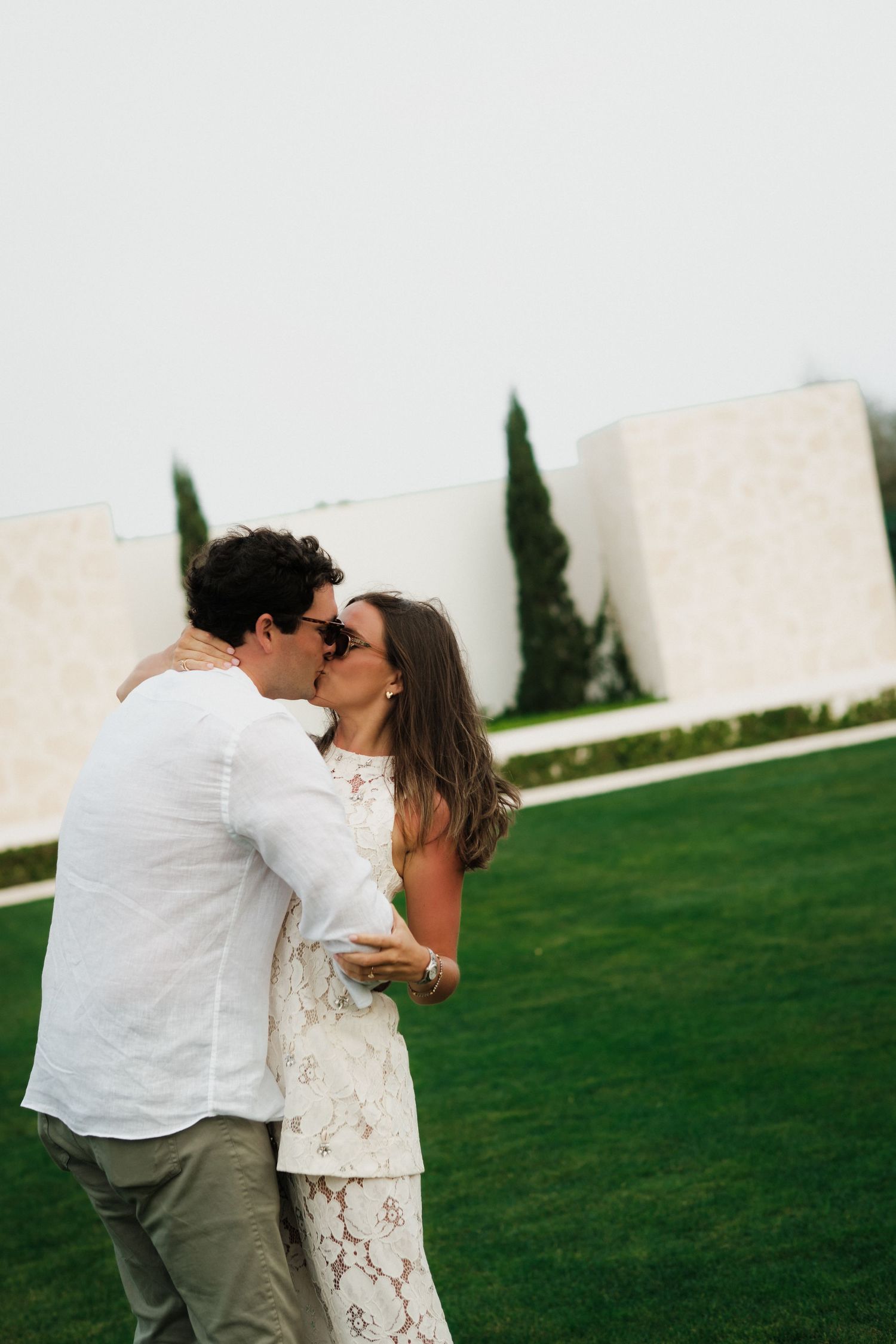 A tender moment between a couple in white clothing on a manicured lawn.