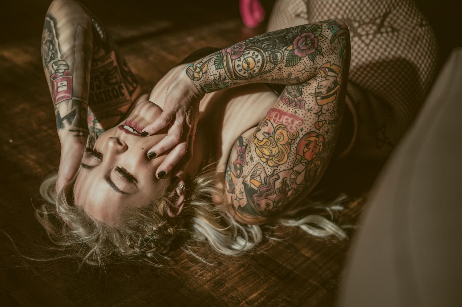 Artistic boudoir photograph showcasing colorful sleeve tattoos in moody lighting.