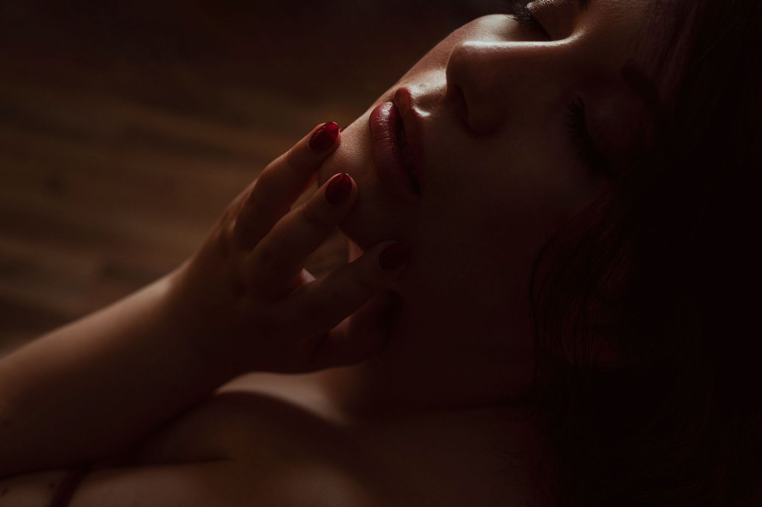 Dramatic low key portrait with soft lighting showing delicate hand gesture against moody dark background.