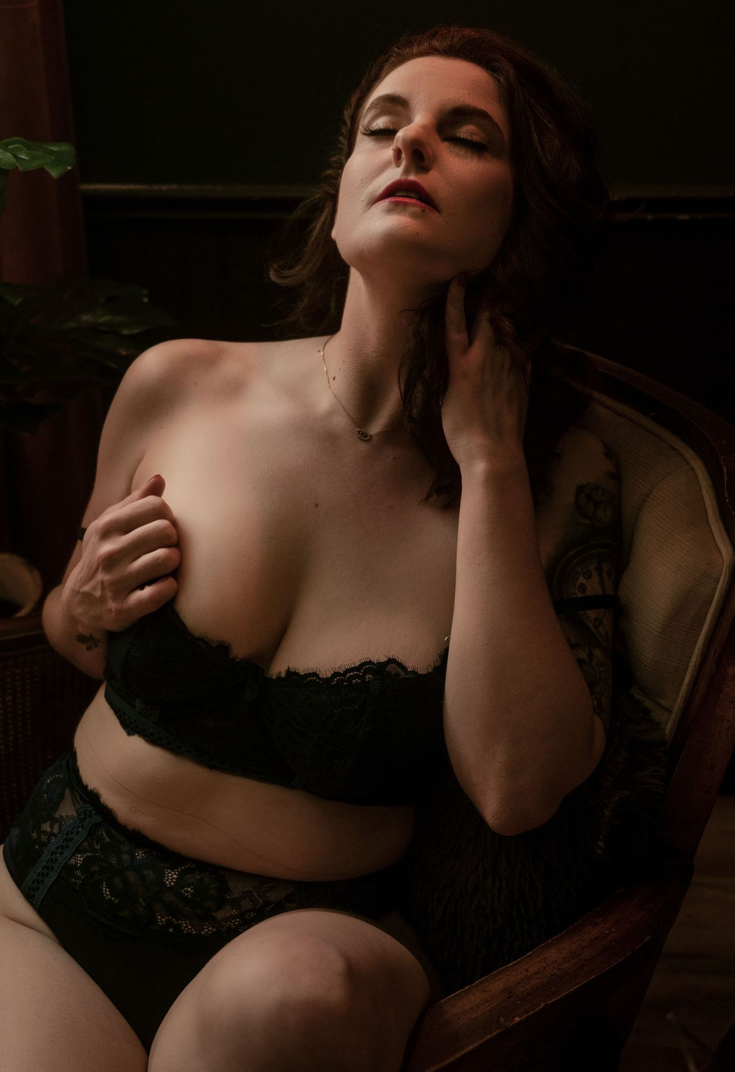 Moody boudoir portrait in black lace against dark background with dramatic lighting.