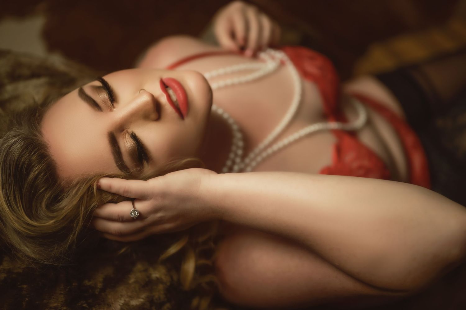 Sensual boudoir portrait on dark fabric with pearl necklace and vintage styling.