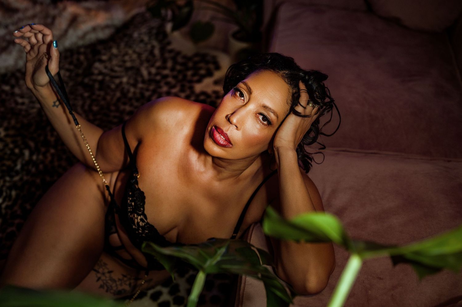 A woman with dark hair reclines on a couch, gazing upward, wearing a black lace top, surrounded by warm, moody lighting.