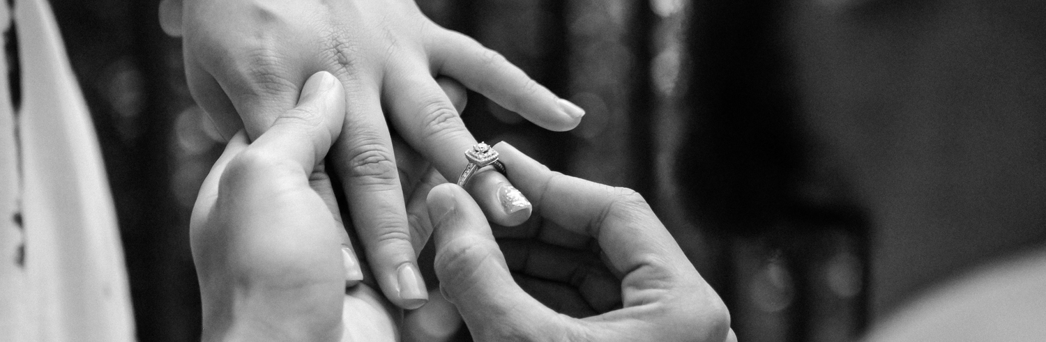 A black-and-white close-up photo of a man putting an engagement ring on a woman's finger.