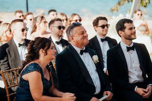 Wedding guests share joyful reactions during an emotional moment at an outdoor ceremony.