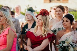 Wedding guests seated outdoors during a ceremony share emotional reactions while watching the proceedings.