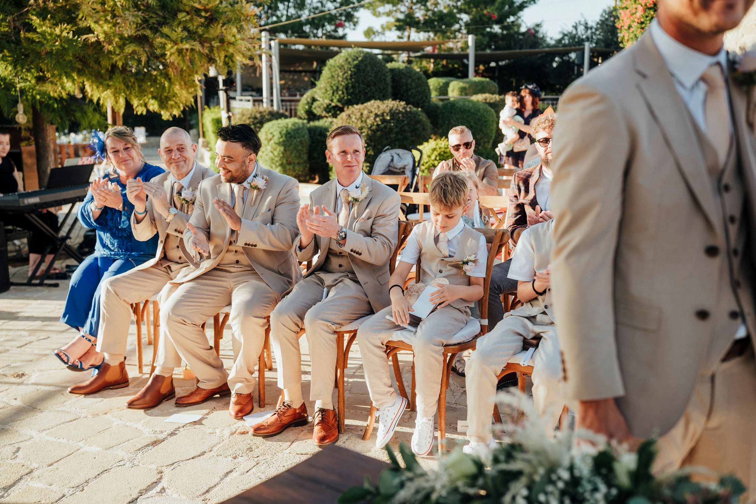 Wedding party members in beige suits sit in a row on outdoor steps showing off their colorful patterned socks.