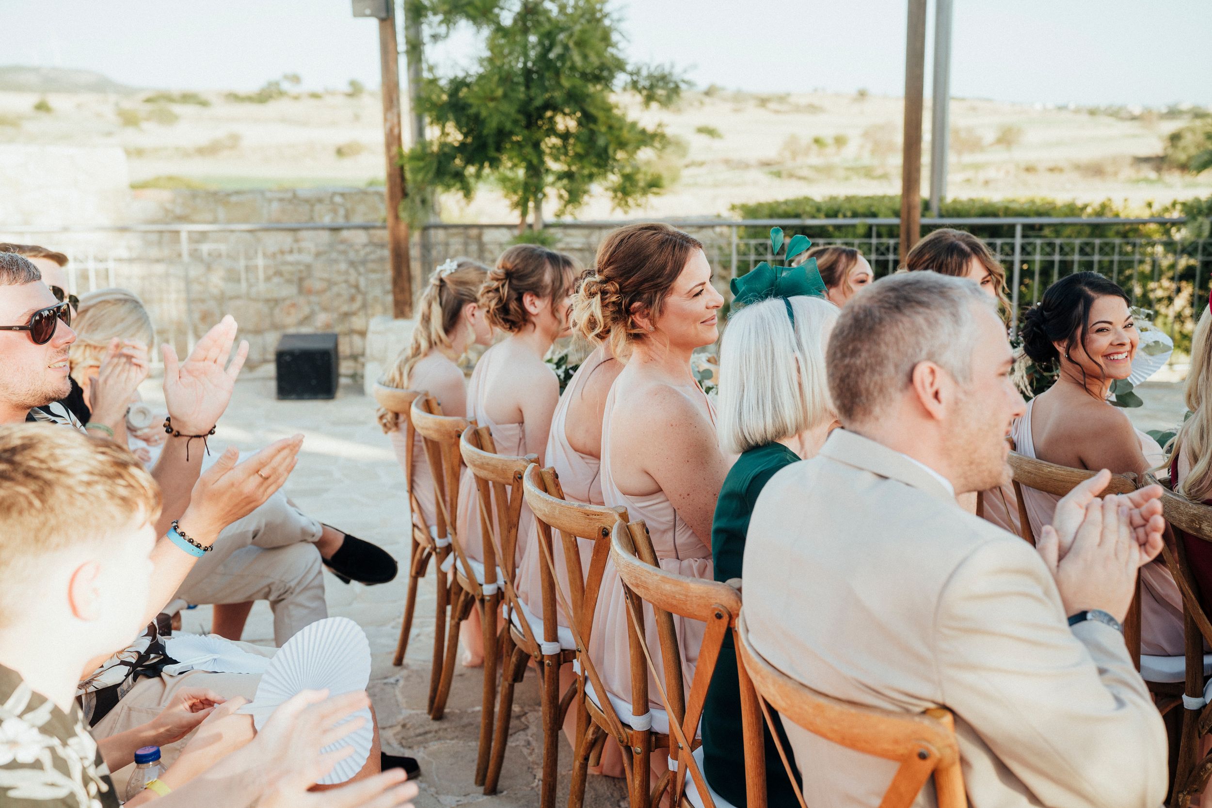 Wedding guests seated at outdoor reception tables with wooden chairs enjoy a sunny desert venue celebration.