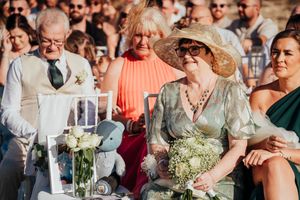 Wedding guests in formal attire seated at an outdoor reception with floral centerpieces and glassware.